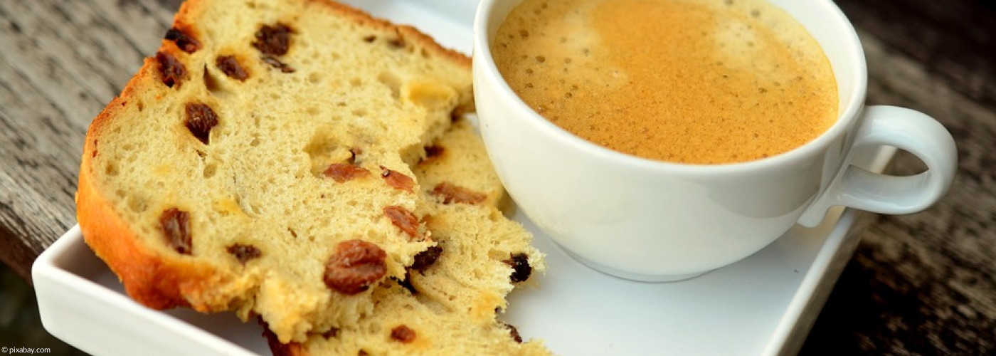 Tasse Kaffe mit einem angebissenen Stück Rosinenbrot