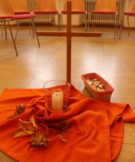 stehendes Kreuz auf orangenen Tuch mit Kerzen und Steinen