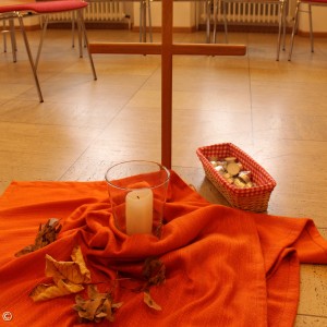 stehendes Kreuz auf orangenen Tuch mit Kerzen und Steinen